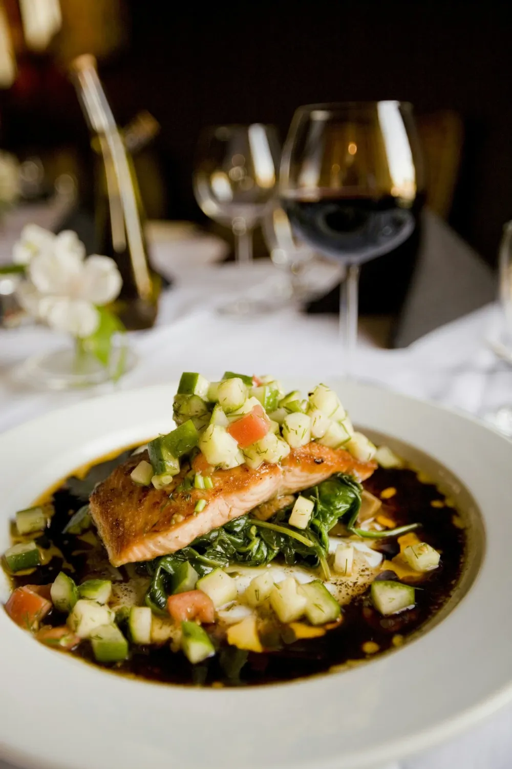 Plated salmon with fresh vegetables beside a glass of red wine