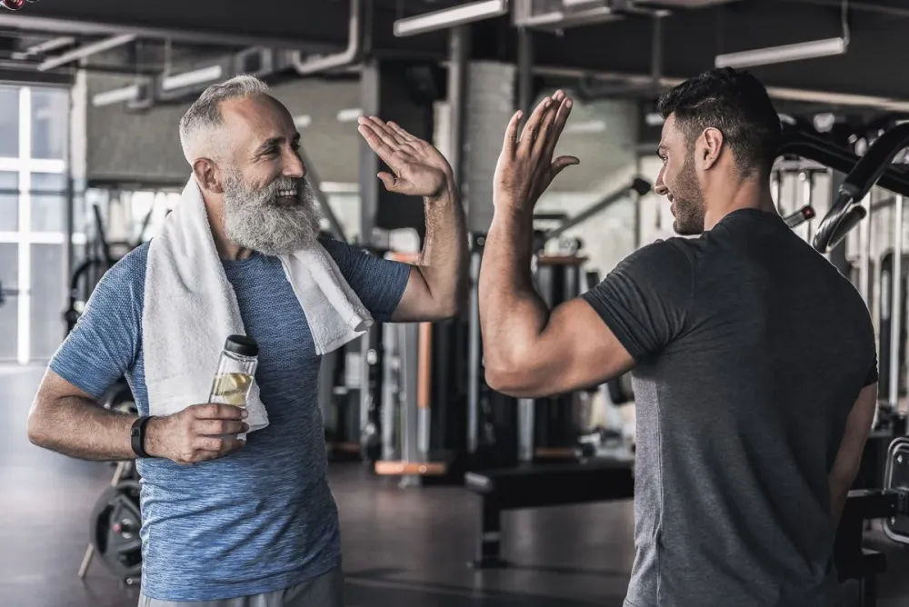 Smiling older man high-fiving his trainer in a gym