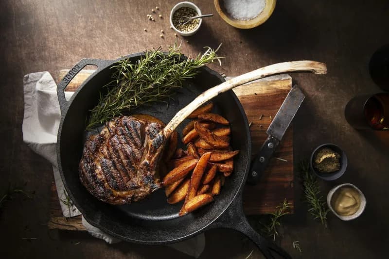 Grilled steak and roasted potatoes in a cast iron pan with fresh herbs