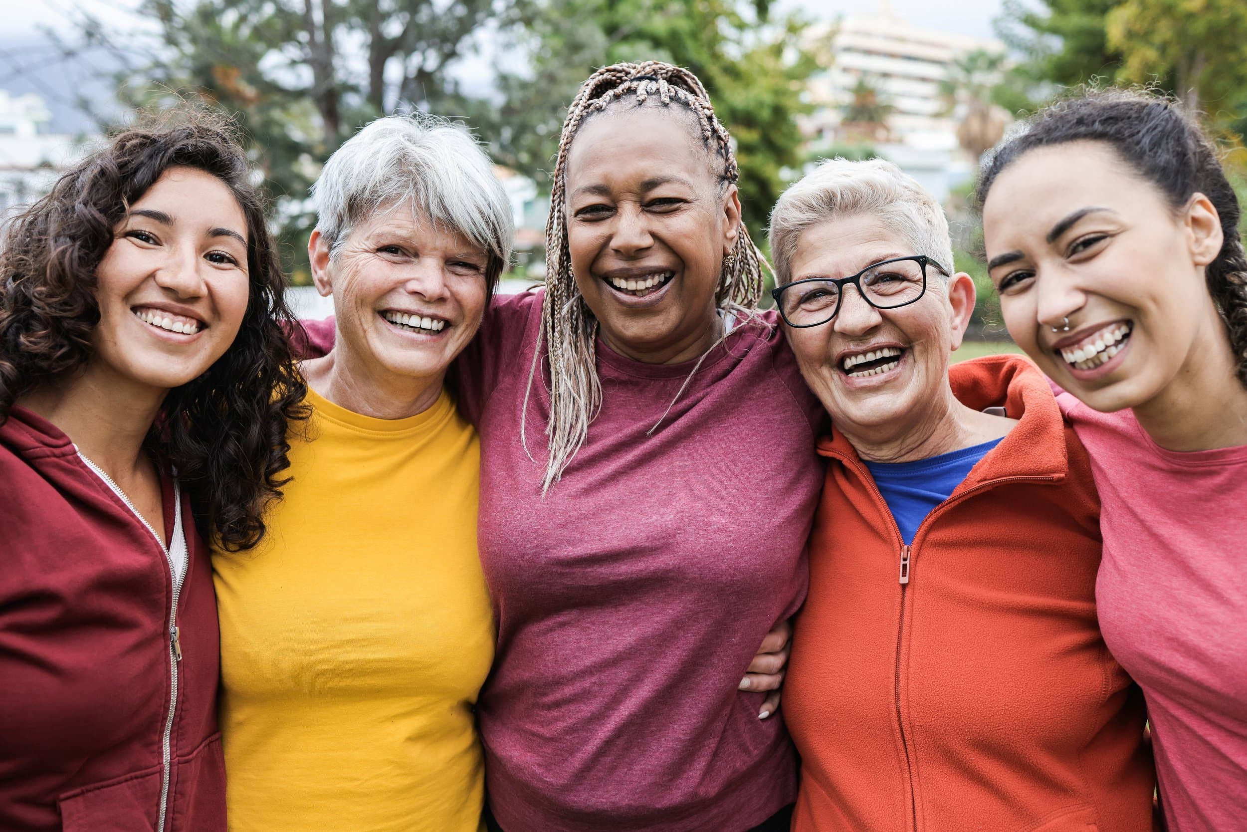 Group of five women smiling and hugging outdoors in a park. Varcity, Purdue University, Texas A&M University, retirement, on campus developments, campus life for life.